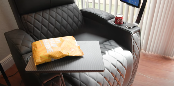 Black leather recliner chair in partially reclined position showing cup holders, center console tray, and yellow pillow on seat